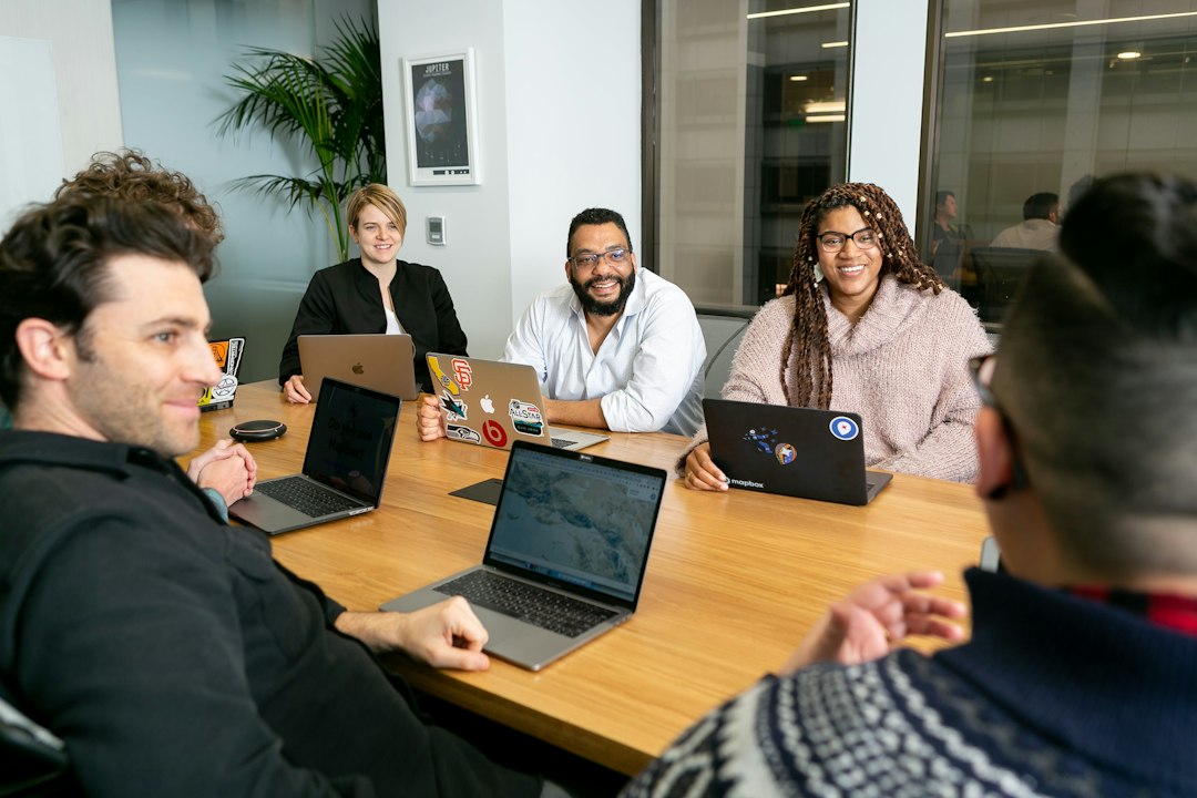 A group of people smiling and collaborating around a table with laptops
